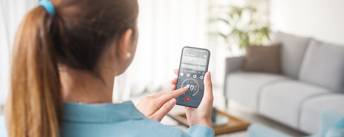 smart thermostat - woman using smart phone app to operate her HVAC unit